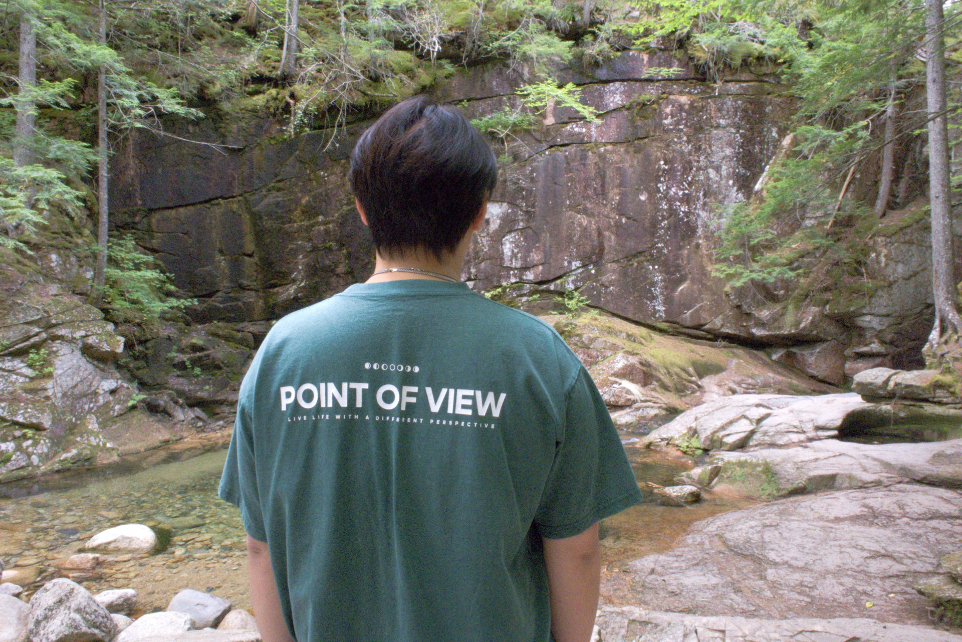 Person wearing a green t-shirt with 'POINT OF VIEW LIVE LIFE WITH A DIFFERENT PERSPECTIVE' on the back. Out doors.