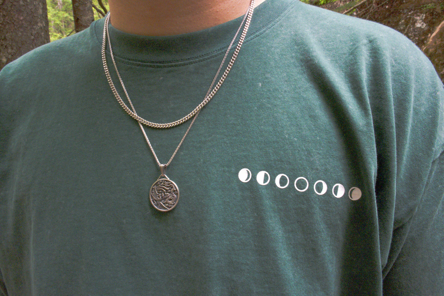 Person wearing a green t-shirt with moon phases. Out doors.