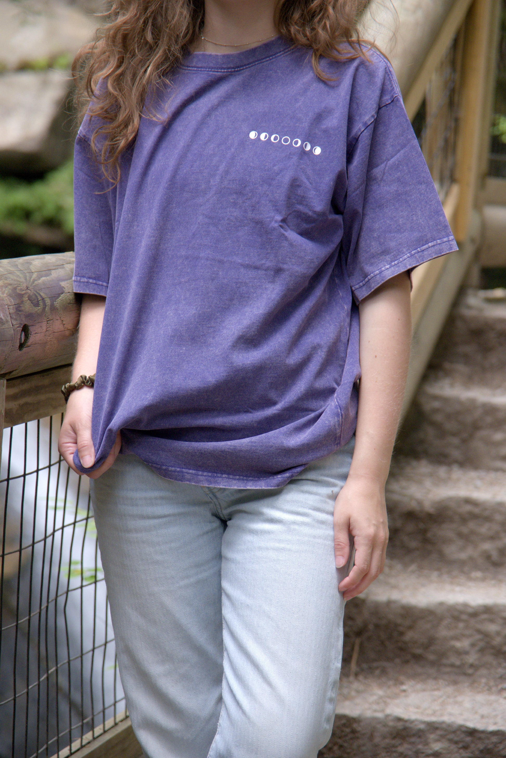 Person wearing a purple t-shirt with moon phases, standing outdoors.
